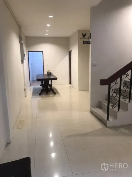 Home Office for rent in Khlong Toei, Bangkok - Long hallway with recessed lights and tiled flooring beside a staircase with wrought-iron balustrade.