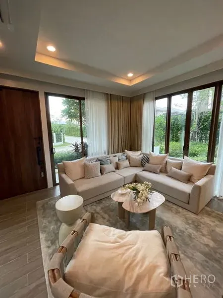 Detached House for sale in Bang Kapi, Bangkok - Bright living room with floor-to-ceiling windows, L-shaped sofa and garden views.