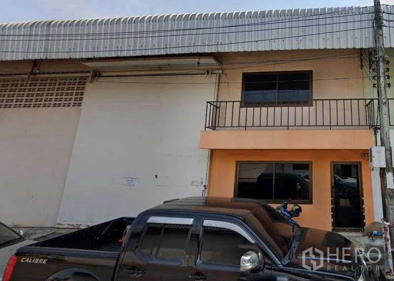 Warehouse for rent in Nong Khaem, Bangkok - Two-storey warehouse facade with balcony, wide windows, and parking space in front.