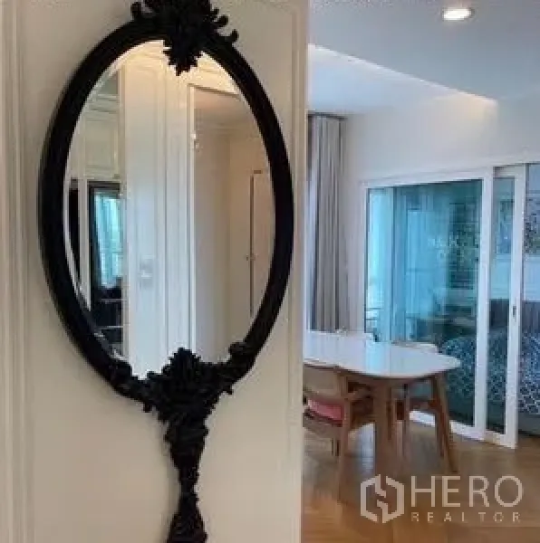 Condominium for rent or sale - Ornate oval wall mirror in a white hallway reflecting the airy dining area and glass doors.