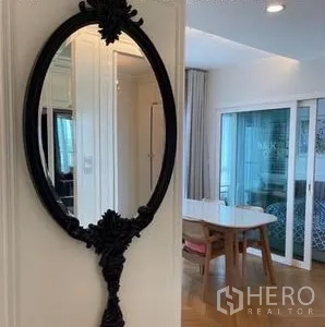 Condominium for rent or sale - Ornate oval wall mirror in a white hallway reflecting the airy dining area and glass doors.