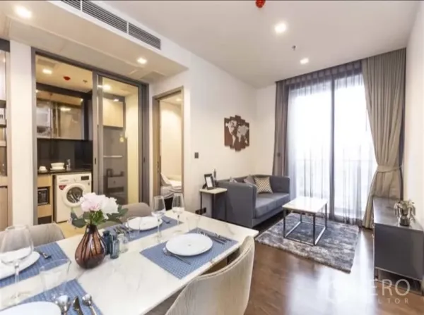 Condominium for rent in Ratchathewi, Bangkok - Bright living and dining area with set table, sofa, balcony doors, and a separate kitchen with washing machine at The Line Ratchathewi.