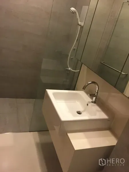 Condominium for rent in Khlong Toei, Bangkok - Contemporary bathroom with glass-enclosed shower, large mirror cabinet and white basin.