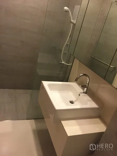 Condominium for rent in Khlong Toei, Bangkok - Contemporary bathroom with glass-enclosed shower, large mirror cabinet and white basin.