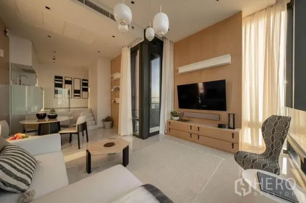 Condominium for rent in Bang Rak, Bangkok - Open living room with TV wall, dining set, and floor-to-ceiling curtains.