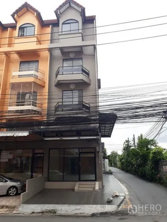 Townhouse for sale in Bang Kapi, Bangkok - Corner townhouse facade with multiple balconies and street-front glass storefront.