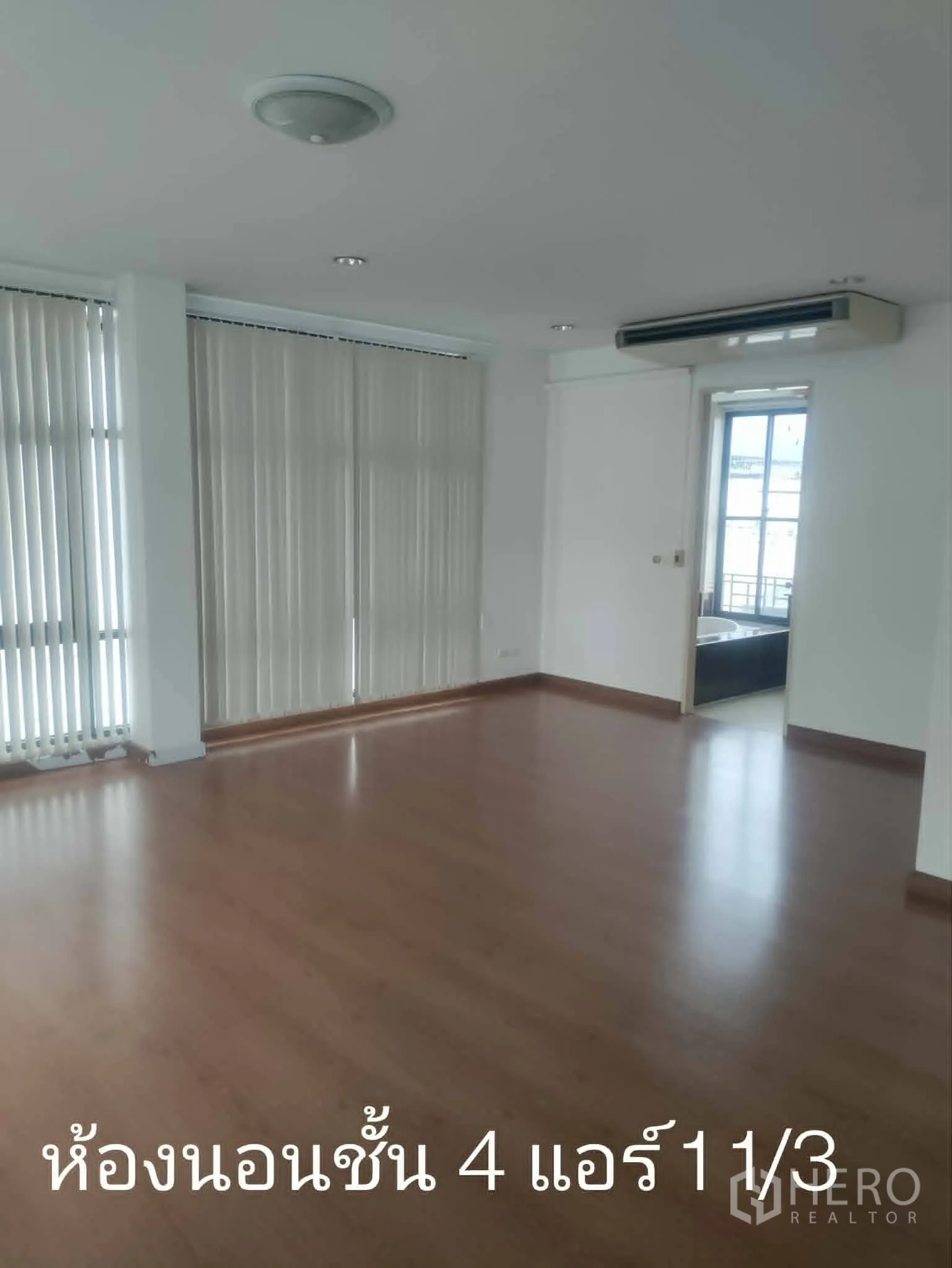 Home Office for rent in Lat Phrao, Bangkok - Spacious room with wood floors, vertical blinds, and wall-mounted air conditioner.