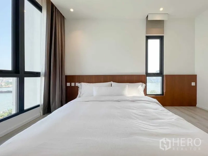 Condominium for rent or sale - Bedroom with bed beside windows overlooking the Chao Phraya River.