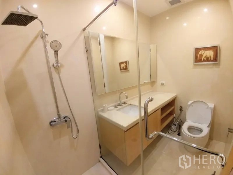 公寓 出租在Chatuchak, Bangkok - 现代浴室，玻璃淋浴间配顶喷花洒，大镜面与洗手台及坐便器。