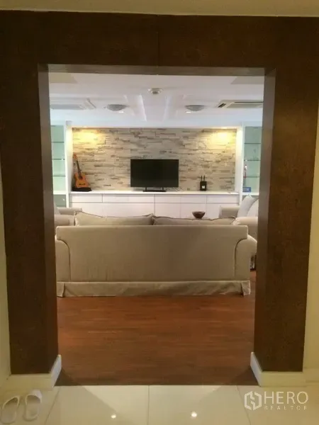 公寓 出租在Khlong Toei, Bangkok - 宽敞客厅视角，米色沙发、叠石特色墙与电视柜，木质地板温馨大气。