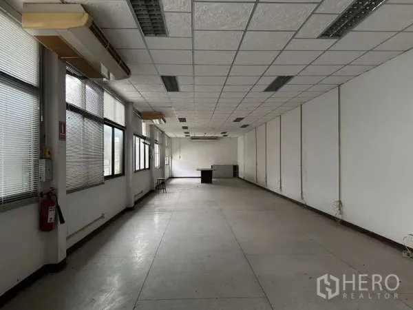 Warehouse for rent in Rat Burana, Bangkok - Long office floor with grid ceiling, fluorescent lighting, and windows with blinds.