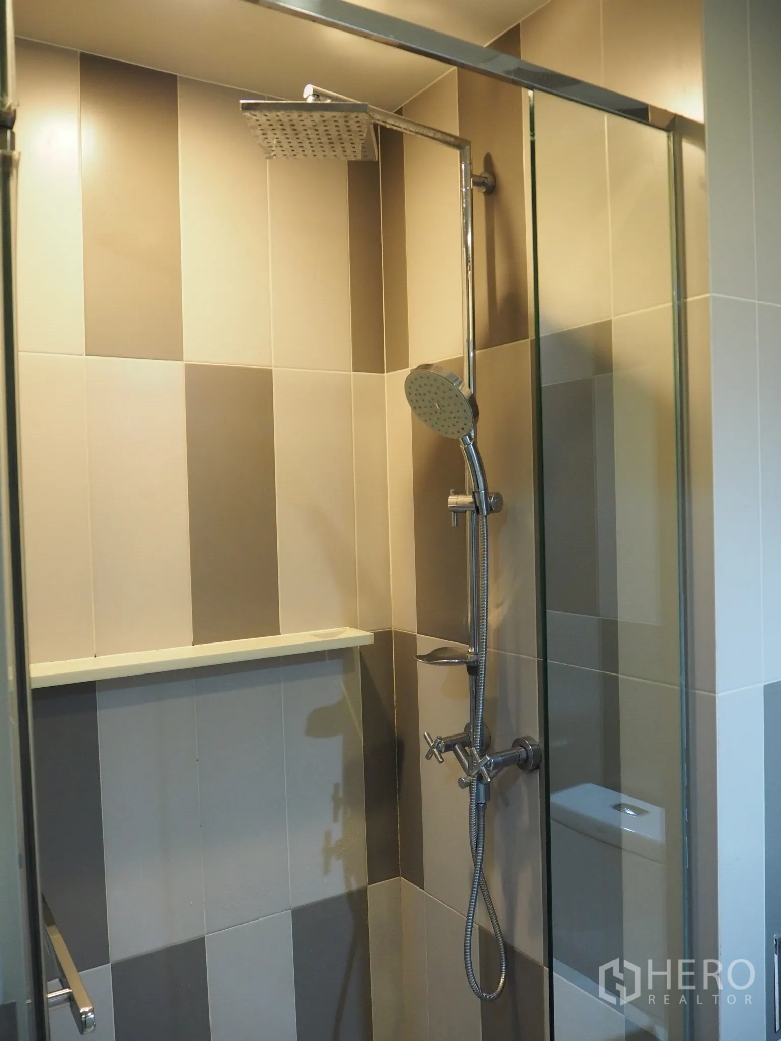 Condominium for rent in Phaya Thai, Bangkok - Glass-enclosed shower with rain showerhead and handheld sprayer against two-tone tiles.