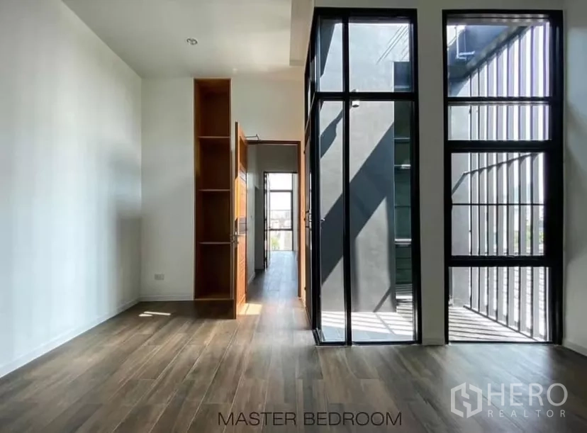 Detached House for rent in Huai Khwang, Bangkok - Master bedroom with floor‑to‑ceiling windows, wood flooring and sliding glass door to balcony.