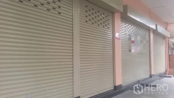 Shophouse for rent in Sathon, Bangkok - Shophouse frontage with multiple beige roll-up metal shutters beneath a covered walkway.