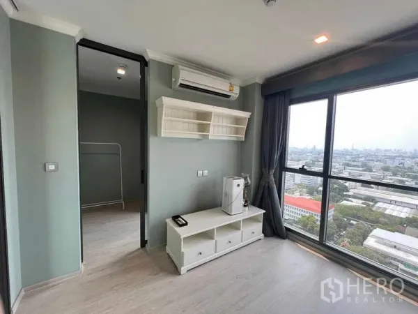 Condominium for sale in Ratchathewi, Bangkok - Bright living area with floor-to-ceiling windows, city skyline view, wall shelves and TV console.
