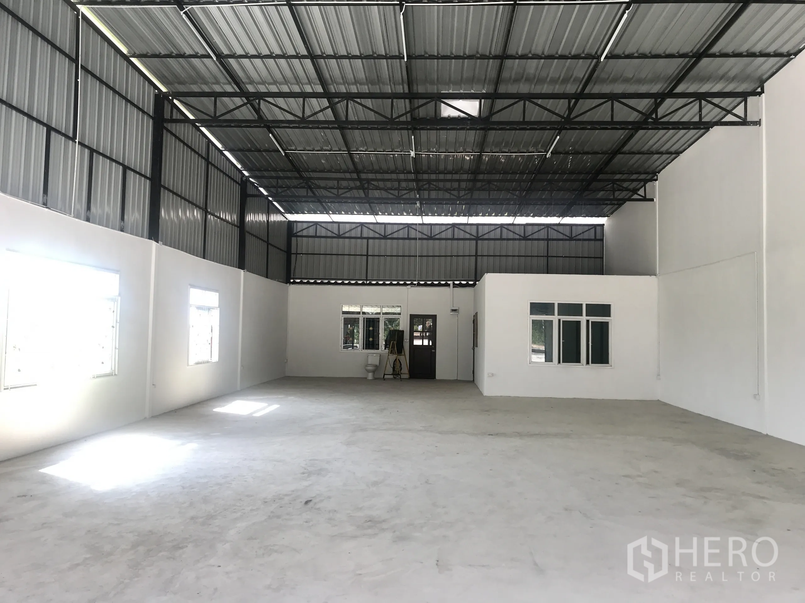 Warehouse for rent in Lam Luk Ka, Pathum Thani - Open‑plan warehouse interior with 6‑meter ceiling, white walls, windows and built‑in office.
