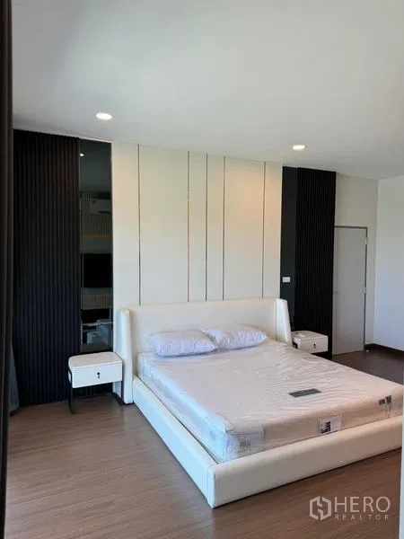 Detached House for rent or sale in Bang Phli, Samut Prakan - Bedroom with white upholstered bed, paneled feature wall, and wood flooring.