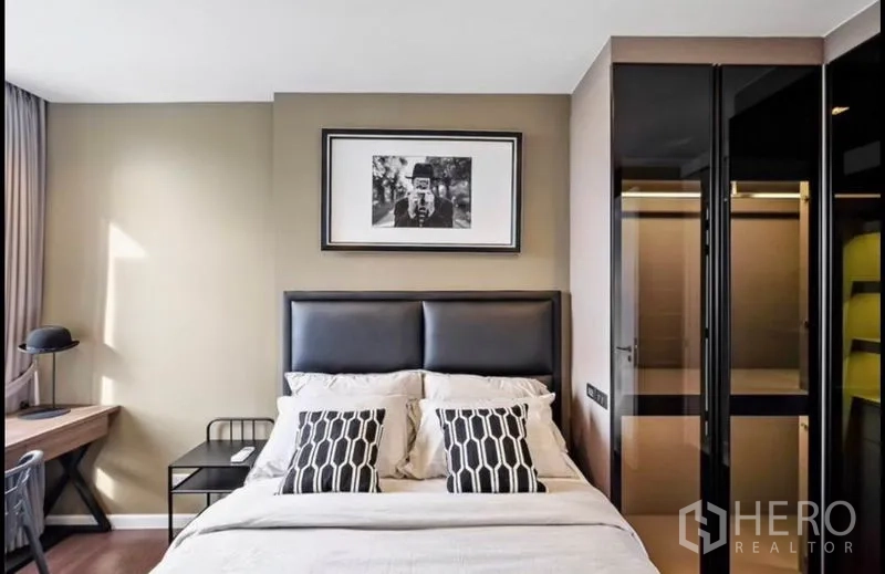 Condominium for rent in Bang Rak, Bangkok - Bedroom with upholstered headboard, study desk and built-in black glass wardrobes.