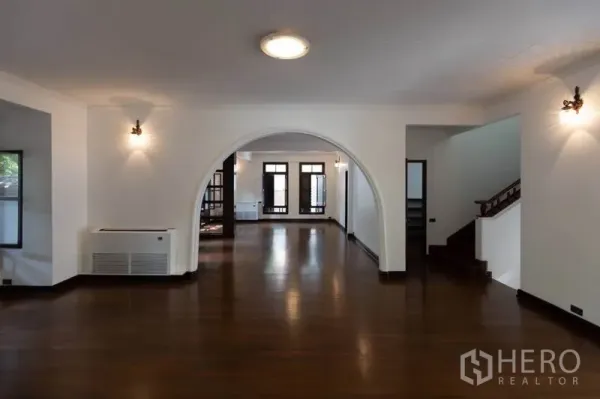 Detached House for rent in Pathum Wan, Bangkok - Spacious living room with archway, dark wood flooring and large windows.