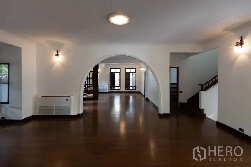 Detached House for rent in Pathum Wan, Bangkok - Spacious living room with archway, dark wood flooring and large windows.