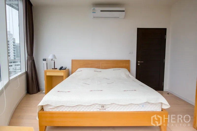 Condominium for rent in Watthana, Bangkok - Minimalist bedroom with a queen bed, wooden furniture, city-facing windows, and a wall-mounted air conditioner.