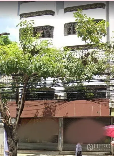 店屋 出租在Watthana, Bangkok - 临街多层商铺外立面，带卷闸门与行道树。