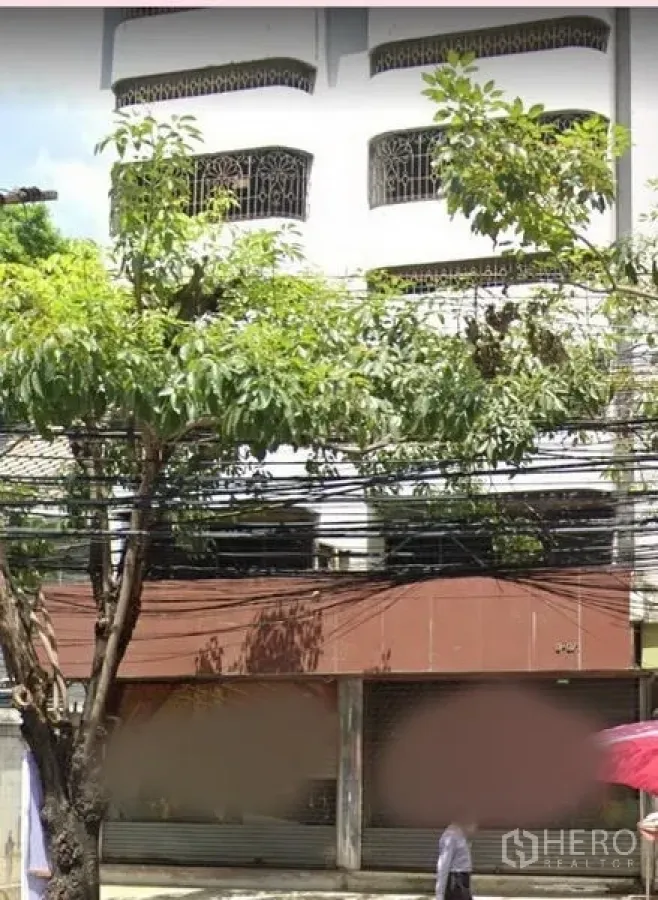 店屋 出租在Watthana, Bangkok - 临街多层商铺外立面，带卷闸门与行道树。