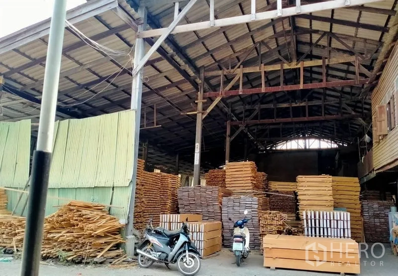 Warehouse for sale in Mueang Nonthaburi, Nonthaburi - High-roof warehouse interior with large stacks of lumber and open loading bay.