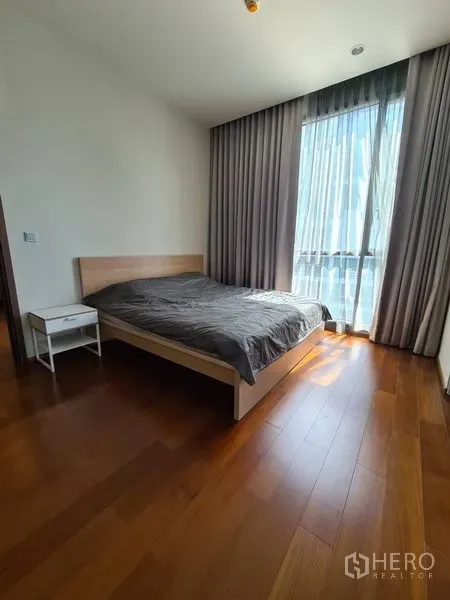 Condominium for rent in Watthana, Bangkok - Bright bedroom with double bed, floor‑to‑ceiling window and wooden flooring.