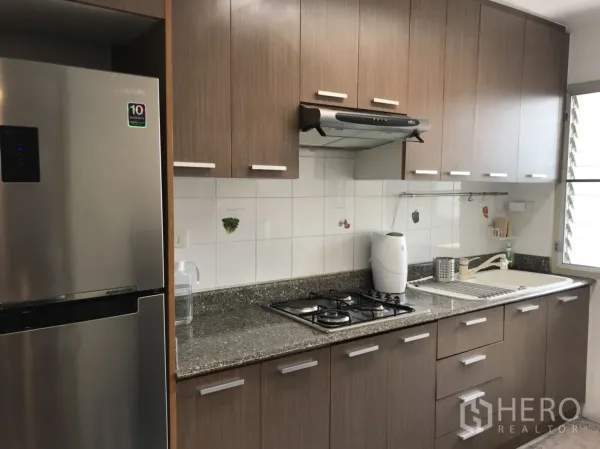 Condominium for rent in Watthana, Bangkok - Fitted kitchen with wooden cabinets, granite countertop, gas hob and stainless refrigerator.