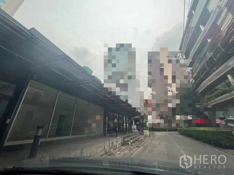 พื้นที่ขายปลีก ให้เช่าในKhlong Toei, Bangkok - แถวอาคารร้านค้าหน้ากระจกพร้อมกันสาดยาวและทางรถผ่าน เห็นตึกสูงย่านพร้อมพงษ์