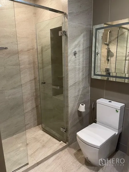 Condominium for rent in Watthana, Bangkok - Modern bathroom with glass shower enclosure, wall mirror and toilet.