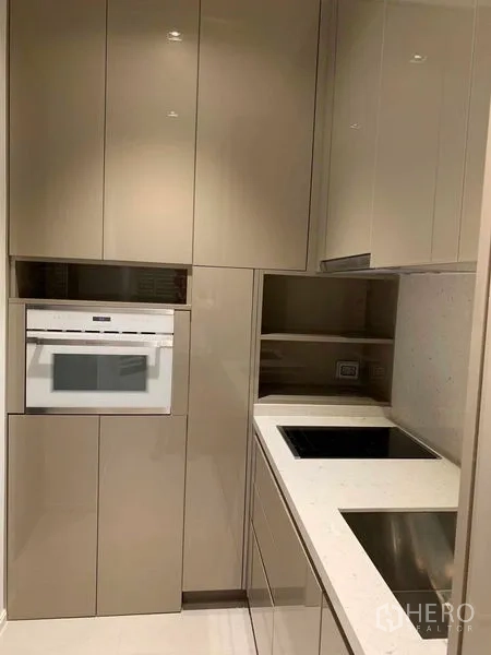 Condominium for rent in Watthana, Bangkok - Compact modern kitchen with glossy cabinets, built-in oven and induction hob.