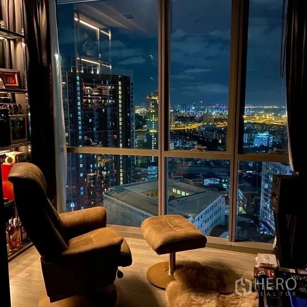 Condominium for rent or sale in Watthana, Bangkok - Night city skyline through corner windows beside a recliner chair.