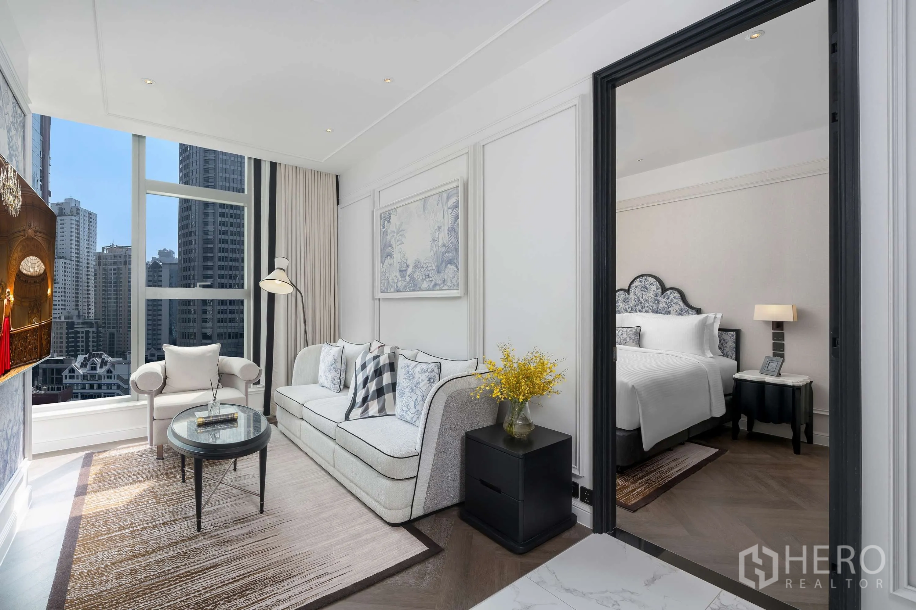 Condominium for rent in Khlong Toei, Bangkok - Elegant living room with sofa, armchair, coffee table, and floor-to-ceiling windows, with bedroom beyond.