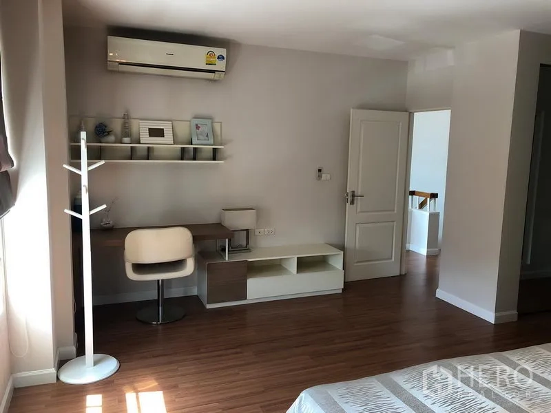 Detached House for rent in Bang Kapi, Bangkok - Spacious bedroom with desk, shelving, air-conditioning and warm wood floors.