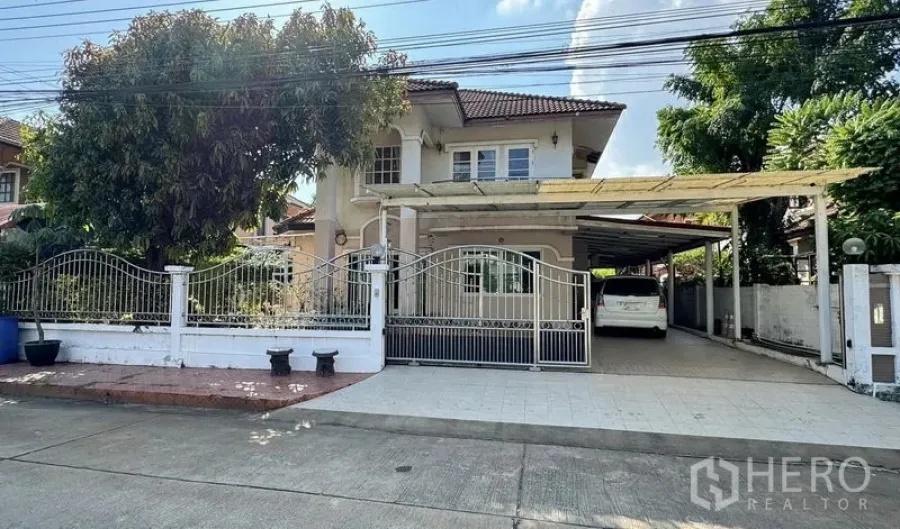 Detached House for sale in Mueang Pathum Thani, Pathum Thani - Street-front view of the two-storey house with gated driveway and multiple covered parking bays.