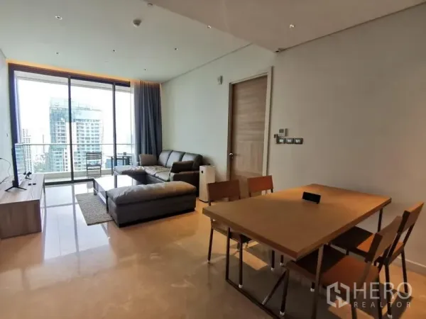 Condominium for rent in Pathum Wan, Bangkok - Bright living and dining area with leather sofa, dining set and floor-to-ceiling windows opening to a balcony with skyline views.