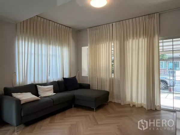 Townhouse for rent in Bang Phli, Samut Prakan - Living area with L-shaped sofa, full-height curtains and access to the patio.