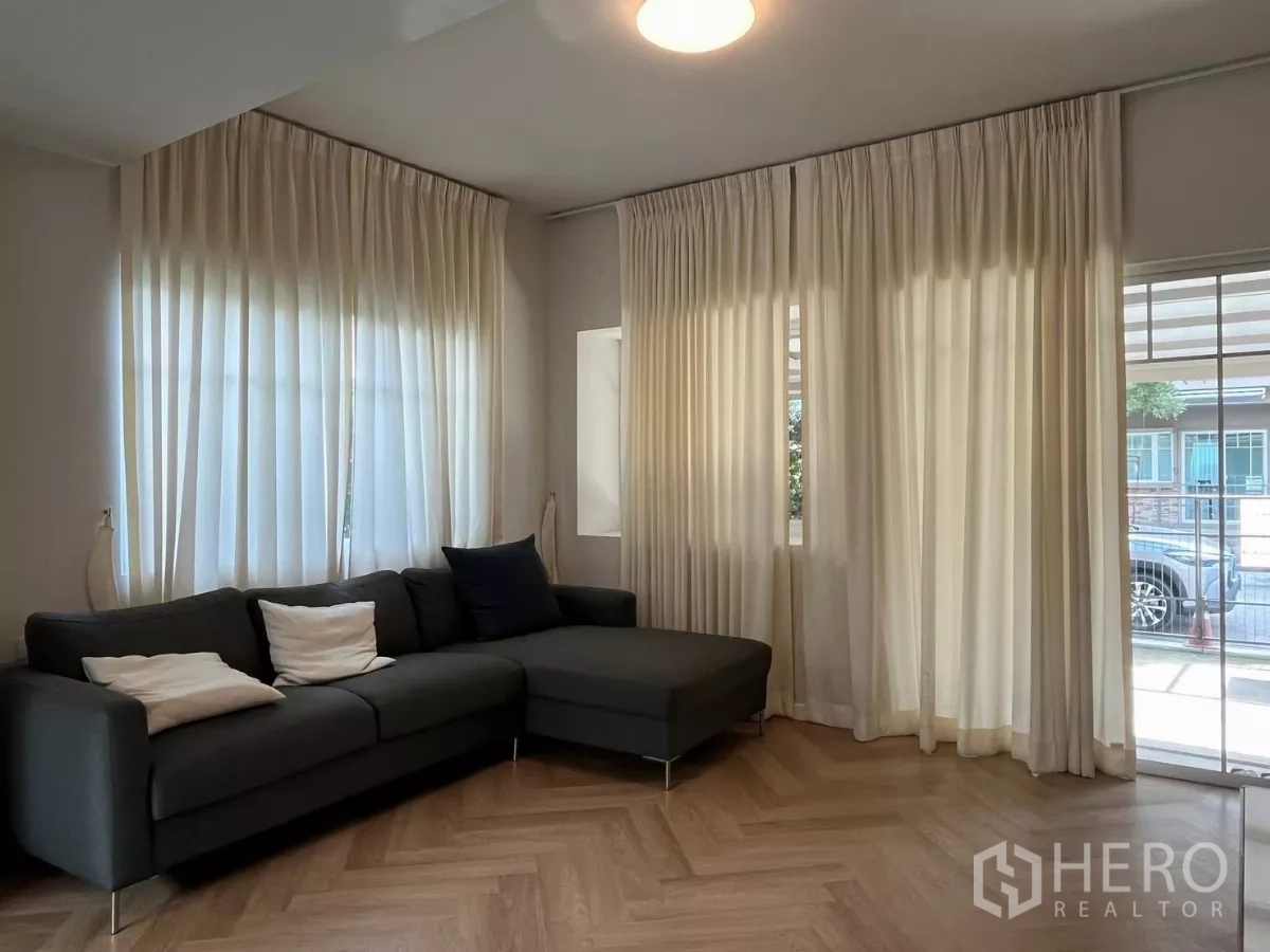 Townhouse for rent in Bang Phli, Samut Prakan - Living area with L-shaped sofa, full-height curtains and access to the patio.