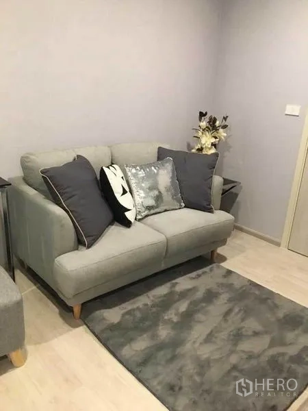 คอนโด ขายในBang Na, Bangkok - อีกมุมของห้องนั่งเล่น แสดงโซฟากะทัดรัดสีเทา หมอนอิง และดอกไม้ตกแต่ง