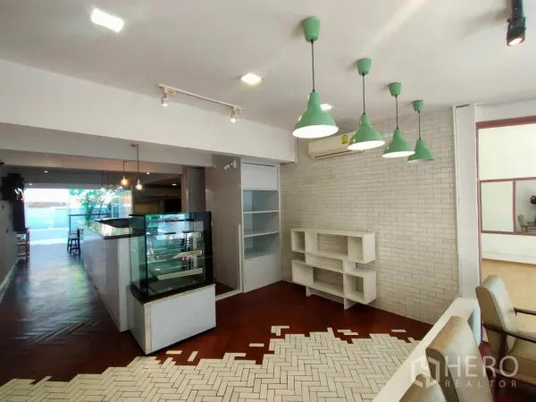 零售空间 出租在Khlong Toei, Bangkok - 明亮店内，白色砖墙、绿色吊灯、展示柜与置物架。