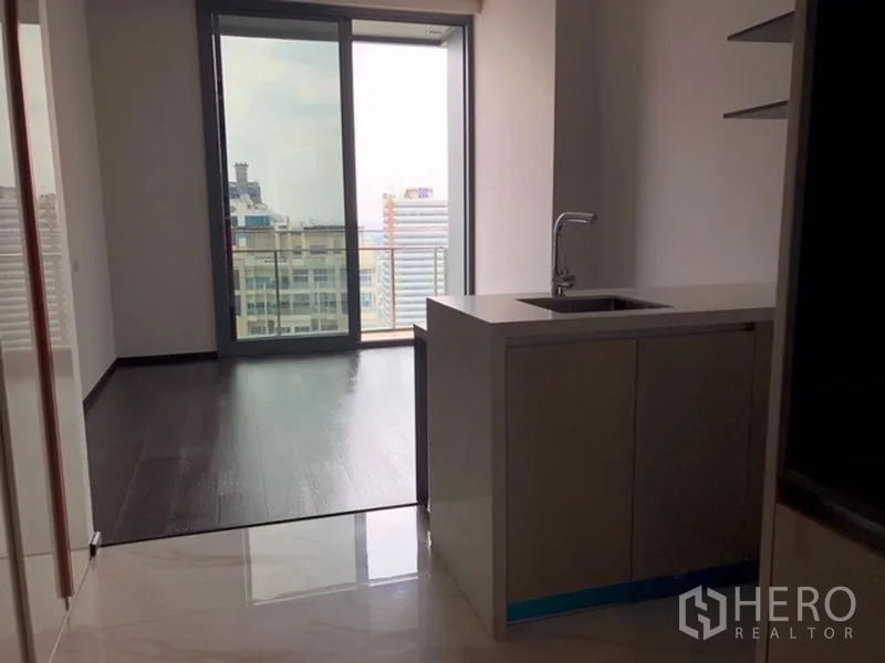 คอนโด ขายในWatthana, Bangkok - พื้นที่นั่งเล่นแบบเปิดพื้นไม้สีเข้ม ครัวขนาดกะทัดรัด และประตูกระจกบานเลื่อนไปยังระเบียงวิวเมือง