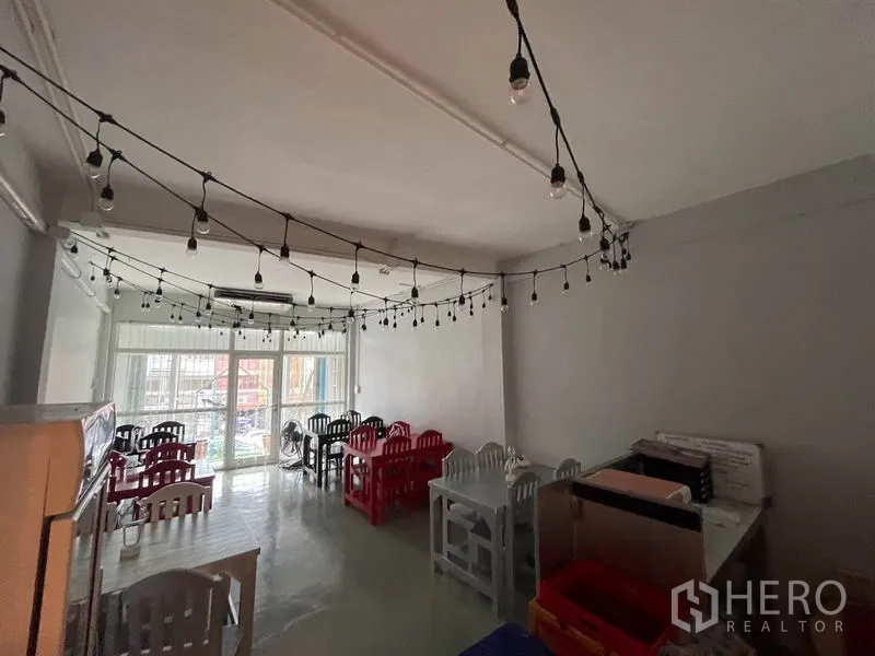 店屋 出租在Ratchathewi, Bangkok - 开放式用餐区，悬挂串灯、彩色桌椅，通向大面积玻璃门。