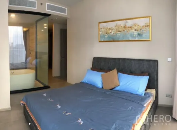 Condominium for rent in Watthana, Bangkok - Cozy master bedroom with blue bedding and a glass-enclosed bathroom featuring a freestanding tub.
