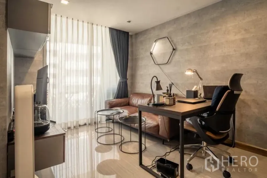 Condominium for sale in Watthana, Bangkok - Living room with leather sofa, work desk and floor-to-ceiling curtains.
