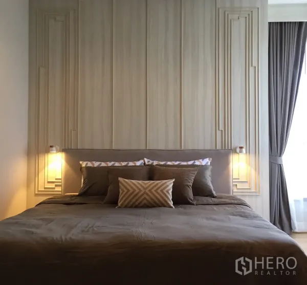 Condominium for rent or sale in Watthana, Bangkok - Spacious master bedroom with king bed, decorative wall panels, twin bedside lamps and blackout drapes.