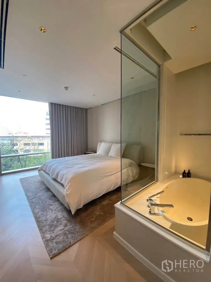 Condominium for rent in Sathon, Bangkok - Master bedroom with king bed and glass-partition bathroom featuring a soaking tub.