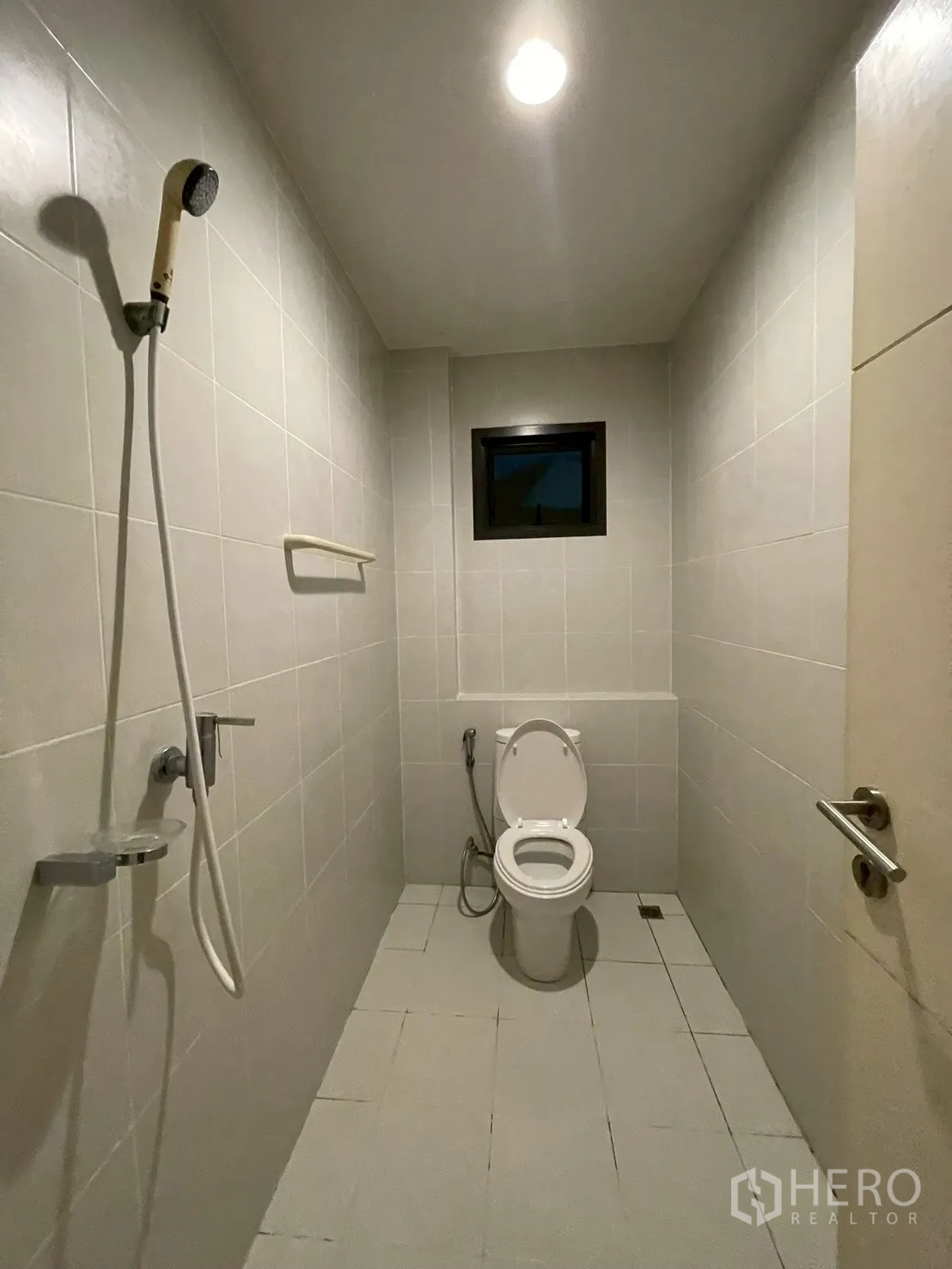 Detached House for rent in Bang Kapi, Bangkok - Tiled bathroom with handheld shower, toilet, and a small window.