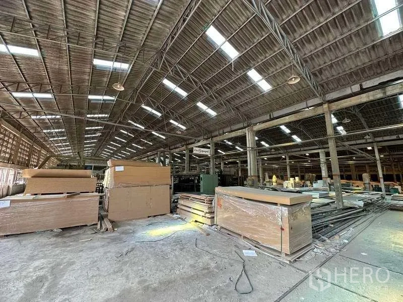 工厂 出租在Sai Noi, Nonthaburi - 工厂内部堆放板材，挑高屋顶，天窗与工业照明。